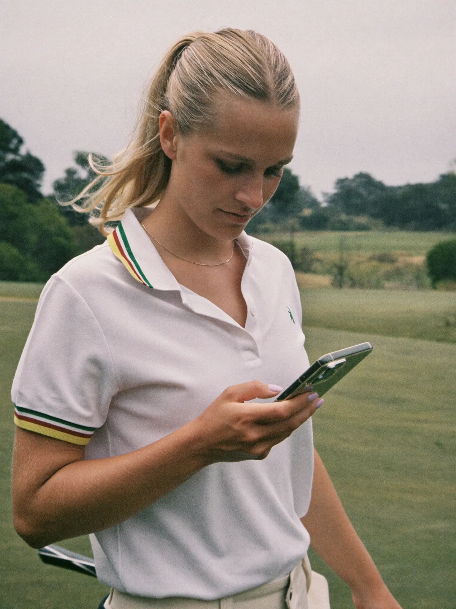 A golfer in a white polo checking her phone on the course