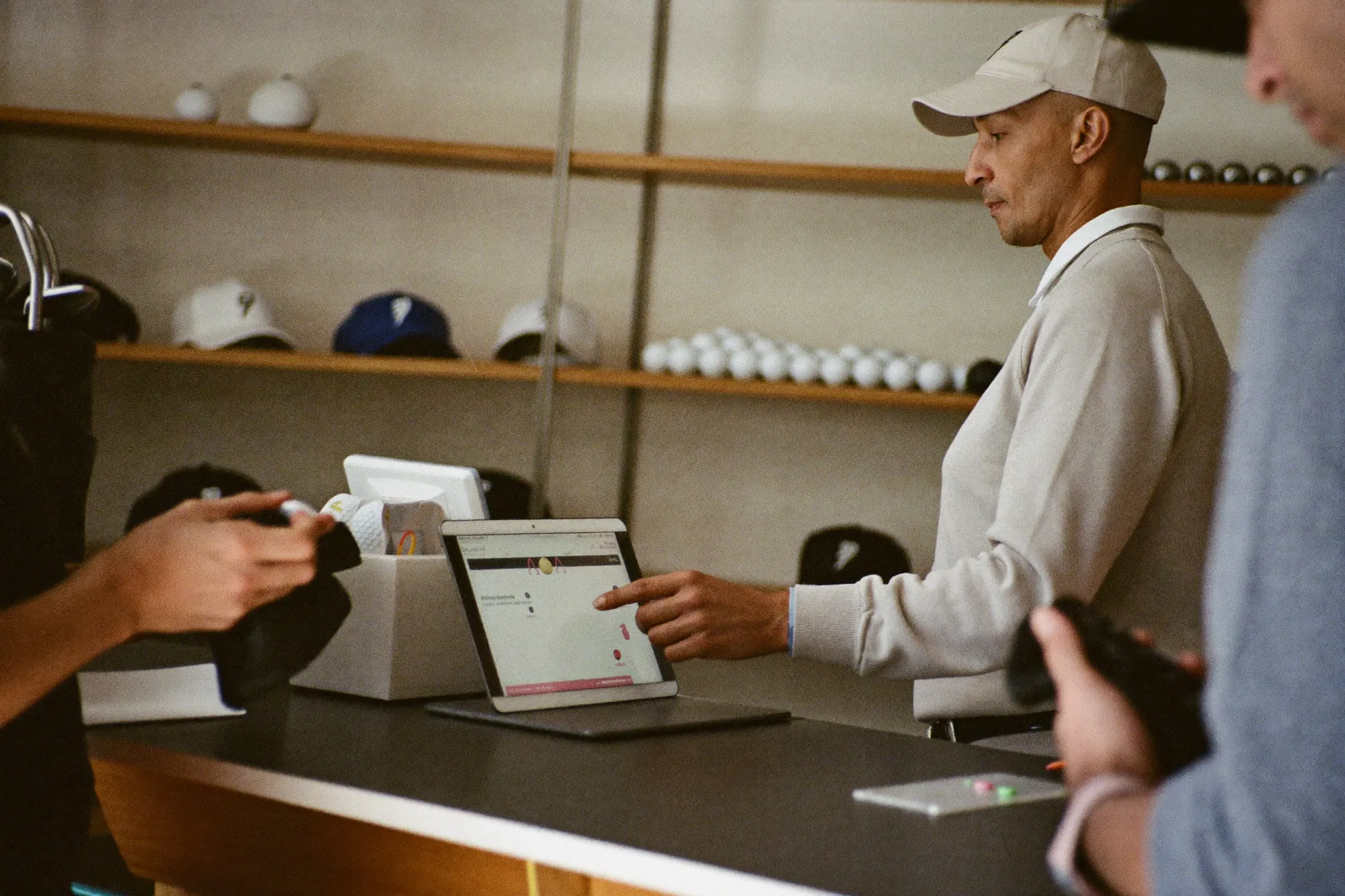 A pro shop attendant ringing up a golfer on a tablet point-of-sale at the counter