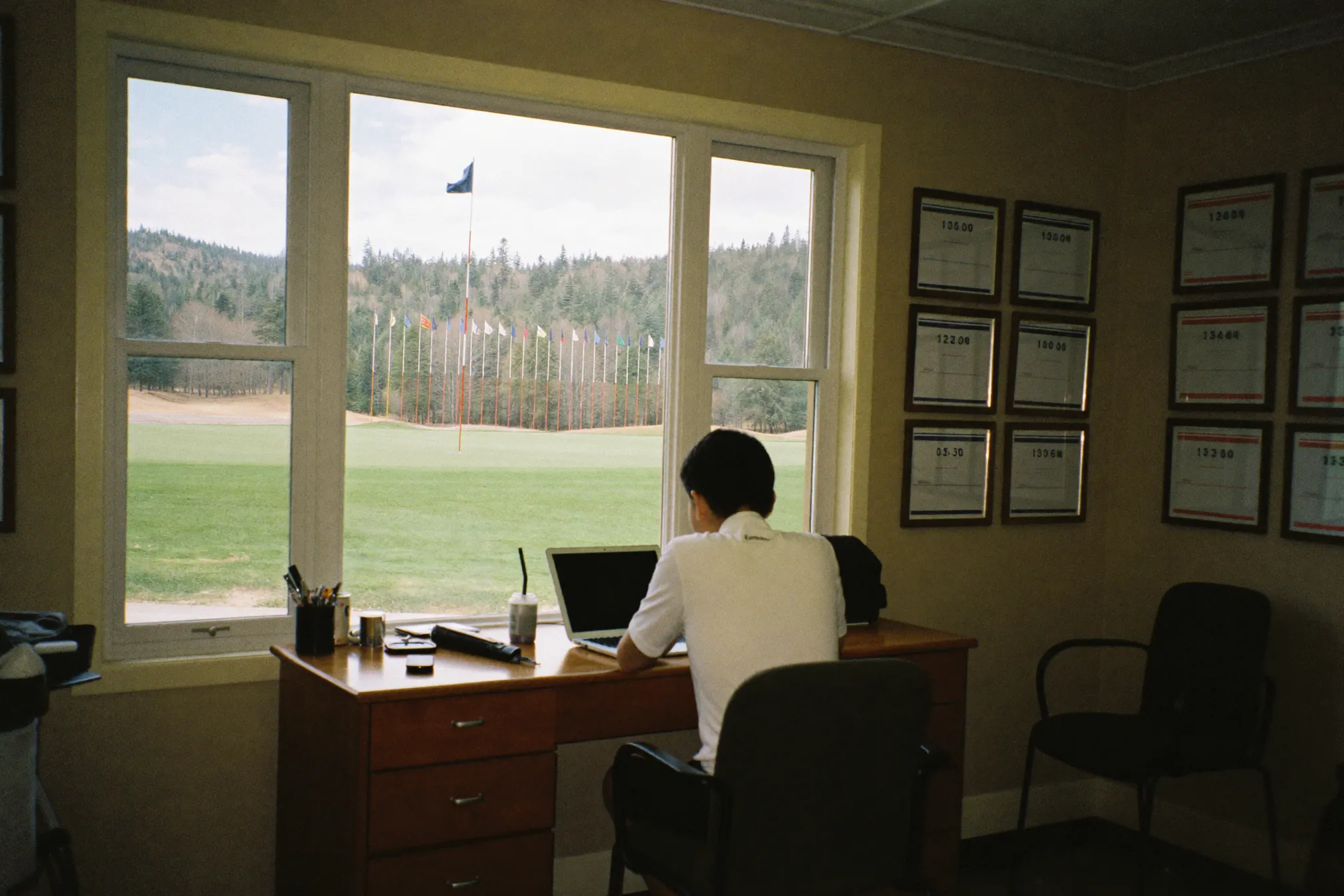 A staff member working on a laptop in a clubhouse office with a window onto the 18th green