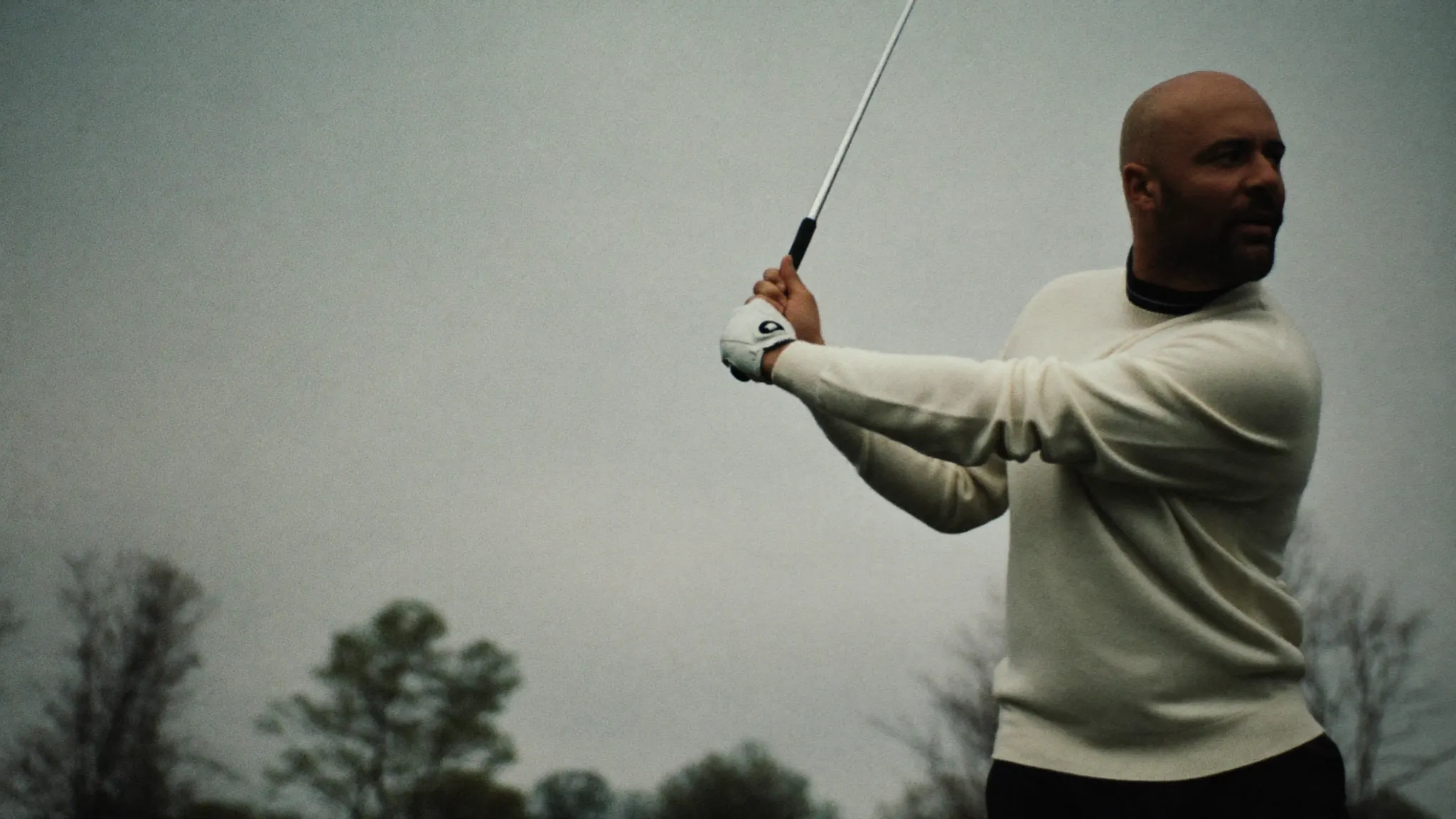A golfer holding his follow-through against an overcast sky